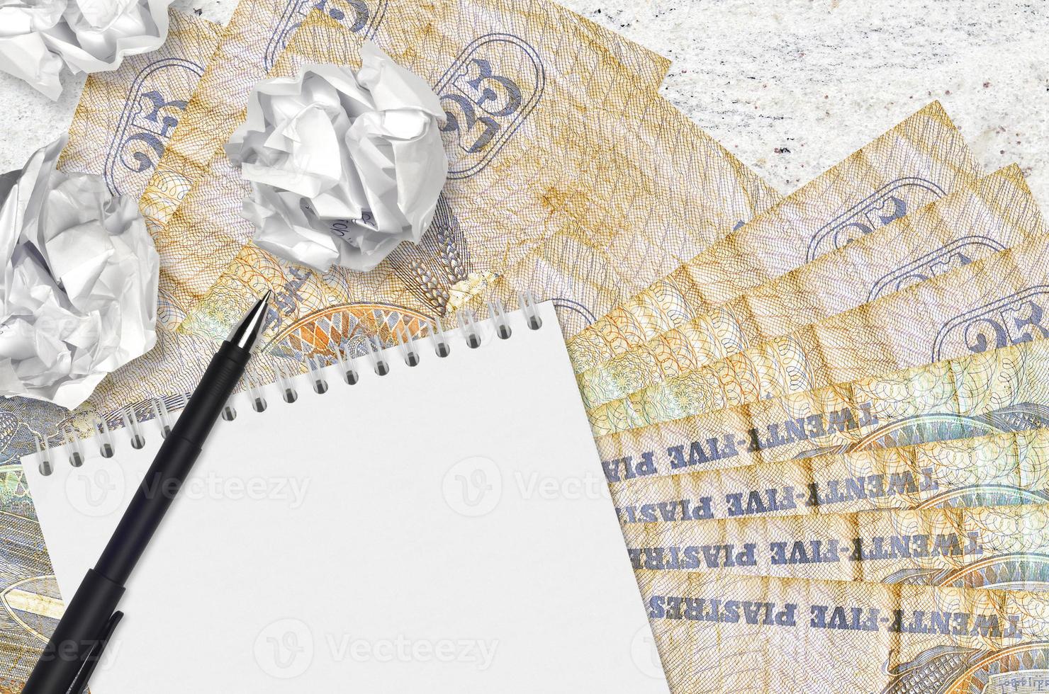 25 Egyptian piastres bills and balls of crumpled paper with blank notepad. Bad ideas or less of inspiration concept. Searching ideas for investment photo