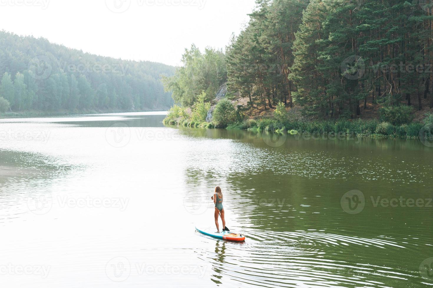 The slim young woman in green sweemsuit on sup boat with oar floating on river, weekend trip and local travel photo