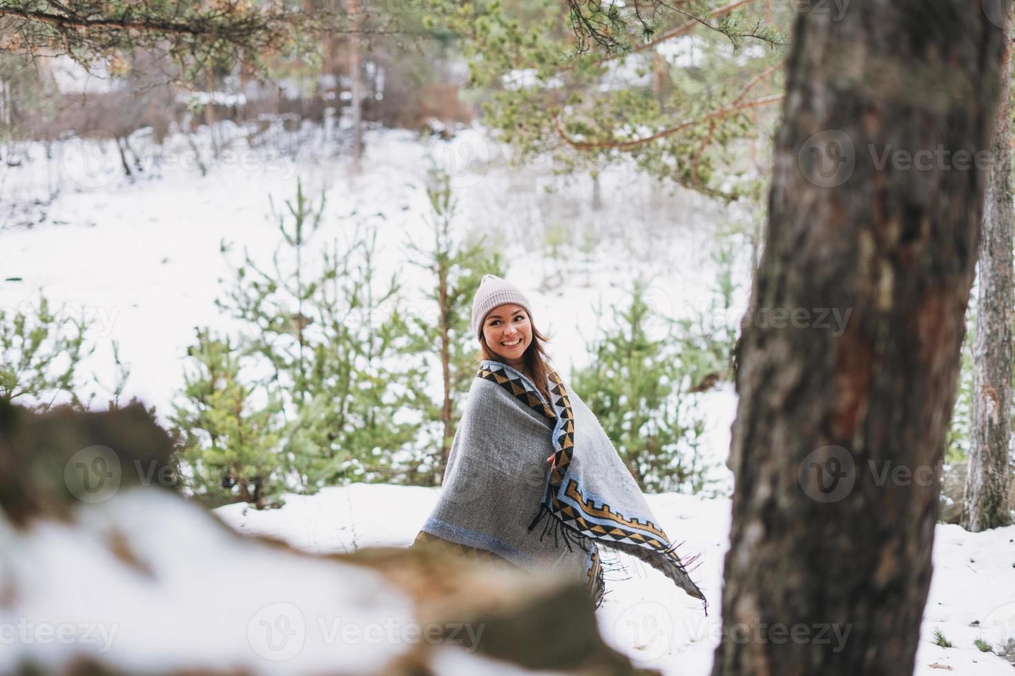 Portrait of young brunette beautiful woman in hat and grey poncho in the winter forest photo