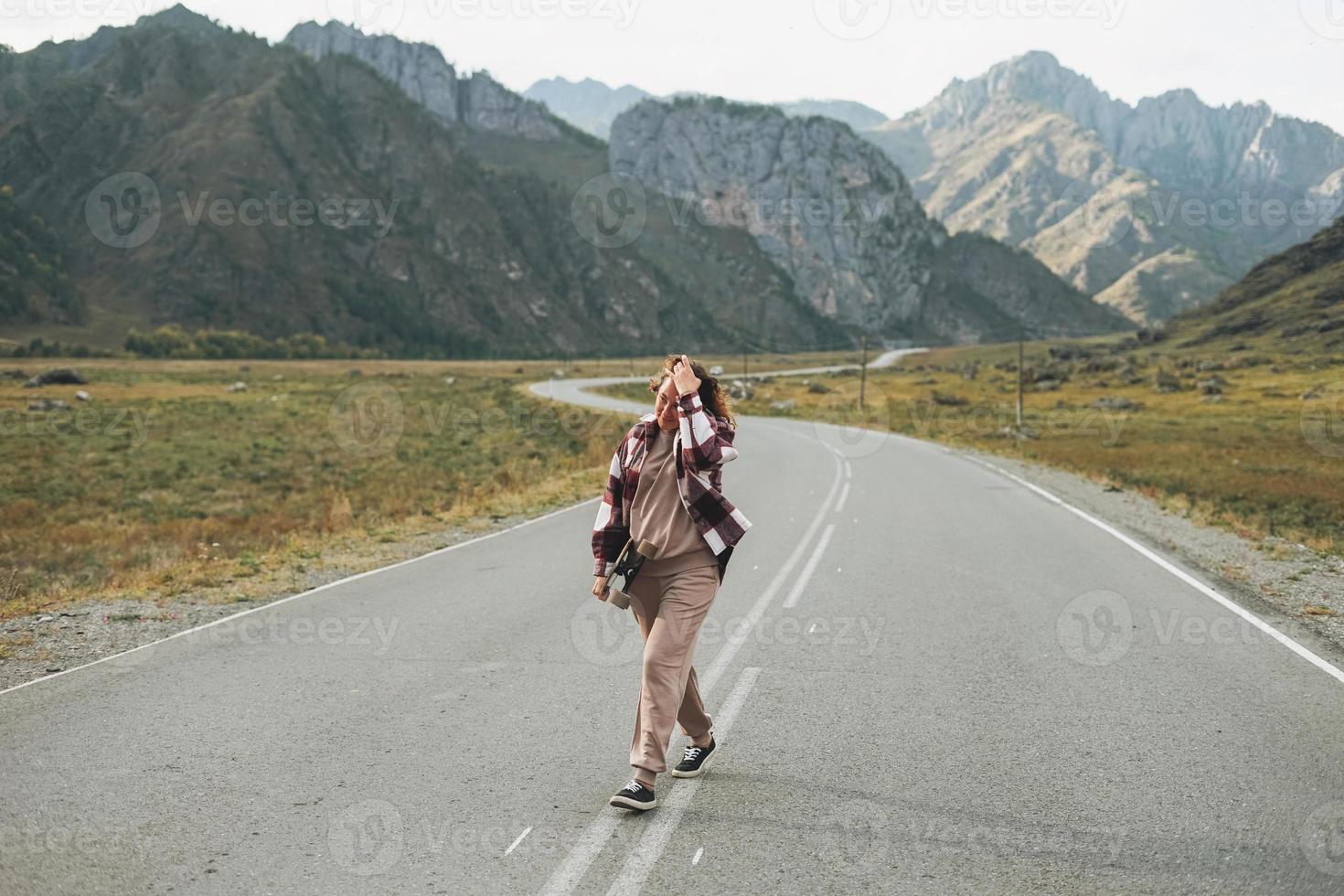 Young woman on skateboard on road against beautiful mountain landscape, Chemalskiy tract, Altai photo