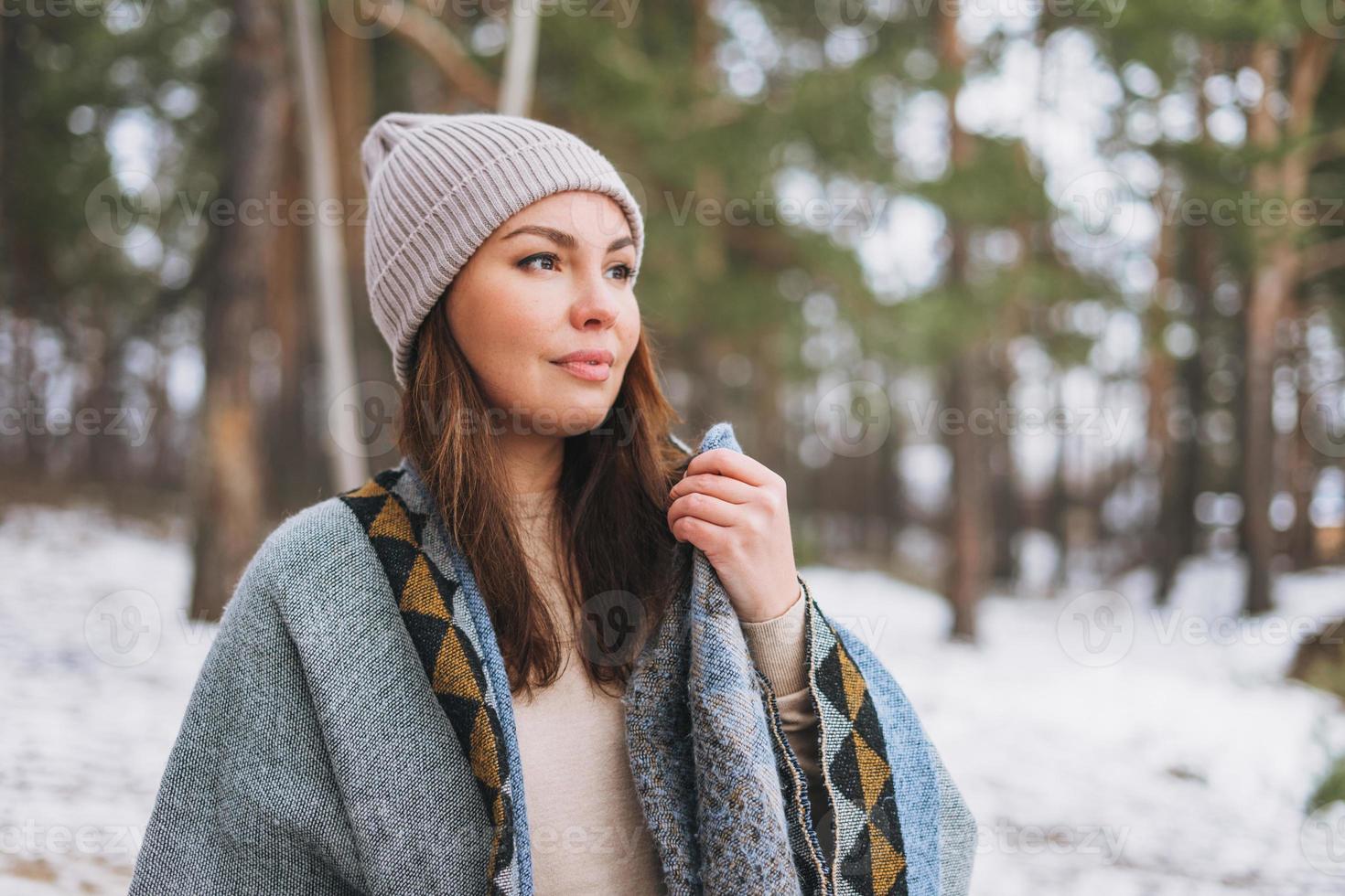 Young brunette beautiful woman in hat and grey poncho in the winter forest photo