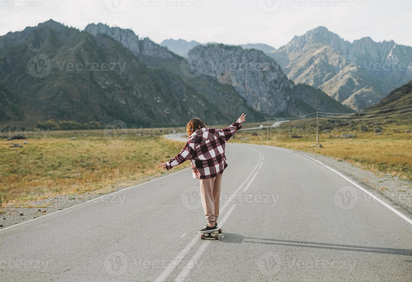 Young woman on skateboard on road against beautiful mountain landscape, Chemalskiy tract, Altai photo