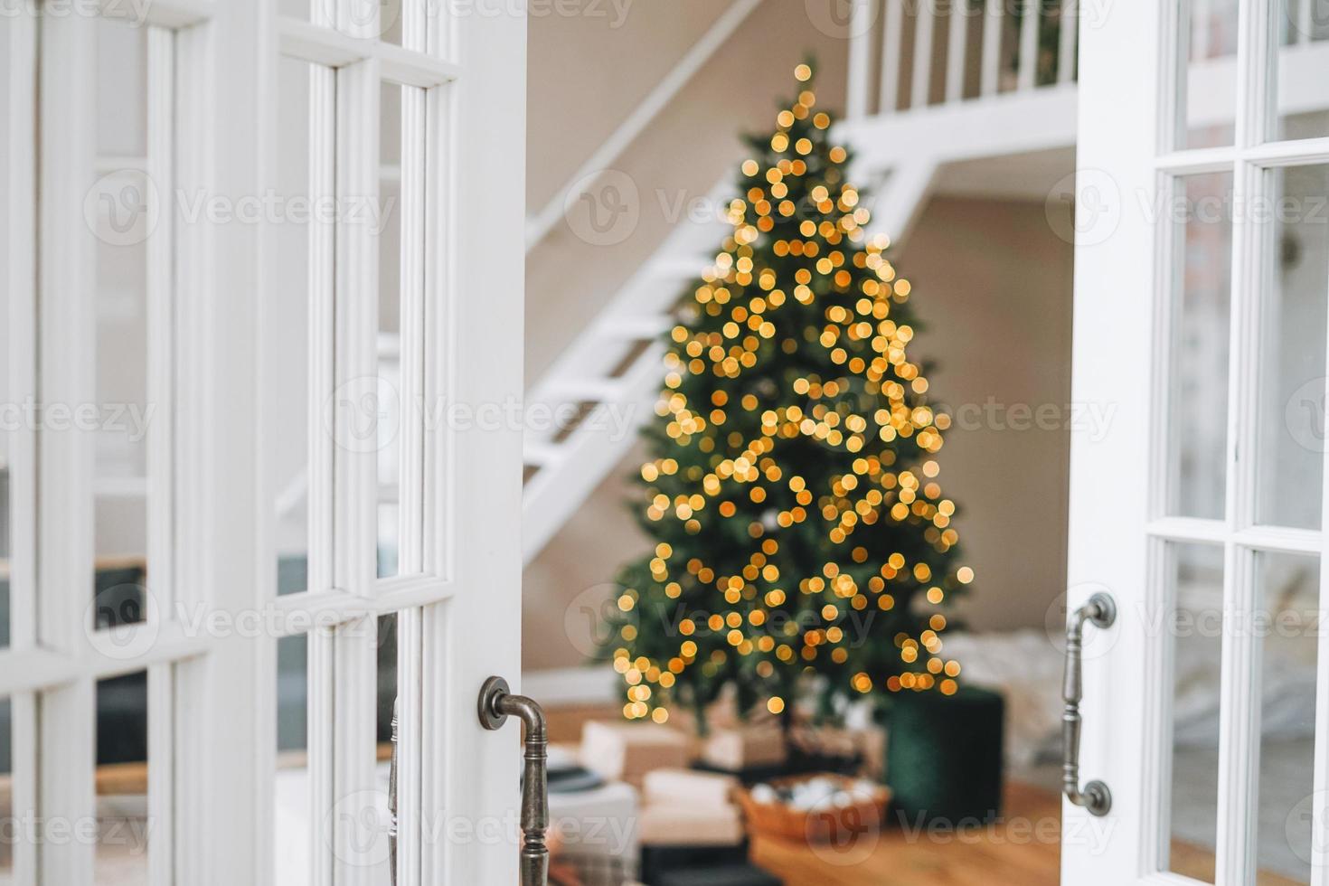 Blurred Decorated Christmas tree with gift boxes from white door at bright interior at the home photo