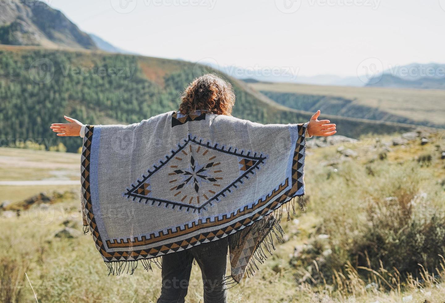 Brunette young woman traveler in poncho from back on road, trip to mountains, Altai photo