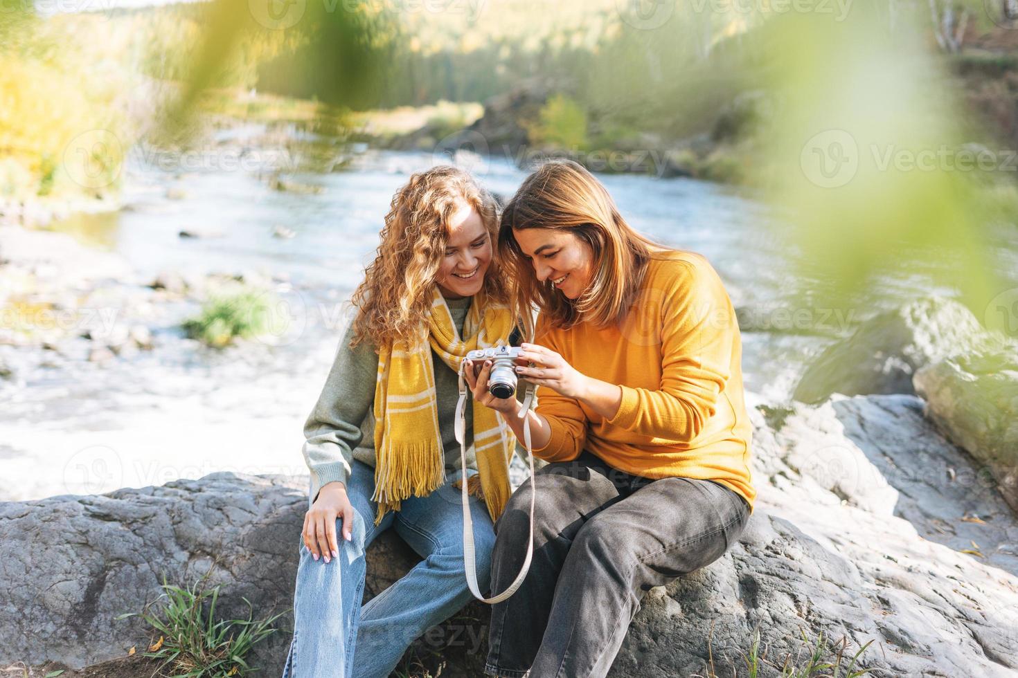 jóvenes mujeres viajeras amigas tomando fotos en la cámara sobre el fondo de la vista de las montañas y el río, caminando en la naturaleza otoñal