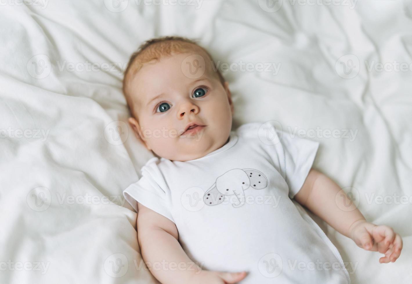 linda niña de 2 a 4 meses en la cama con sábanas blancas, tonos naturales, enfoque selectivo foto