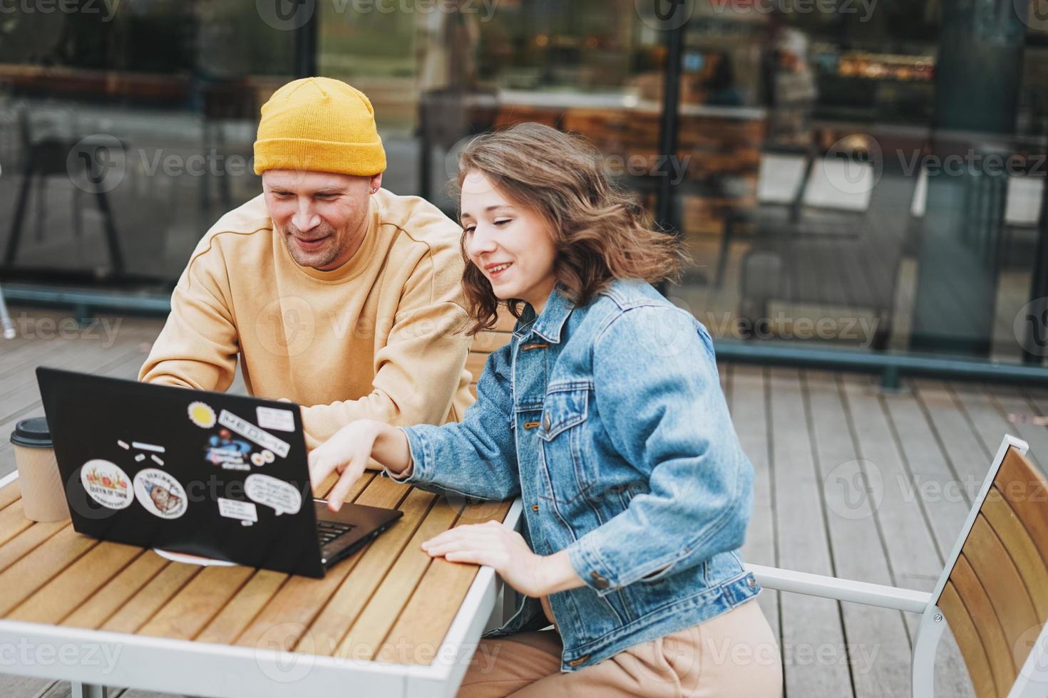 Una pareja joven y elegante que trabaja por cuenta propia trabajando en una laptop en el café de la calle foto