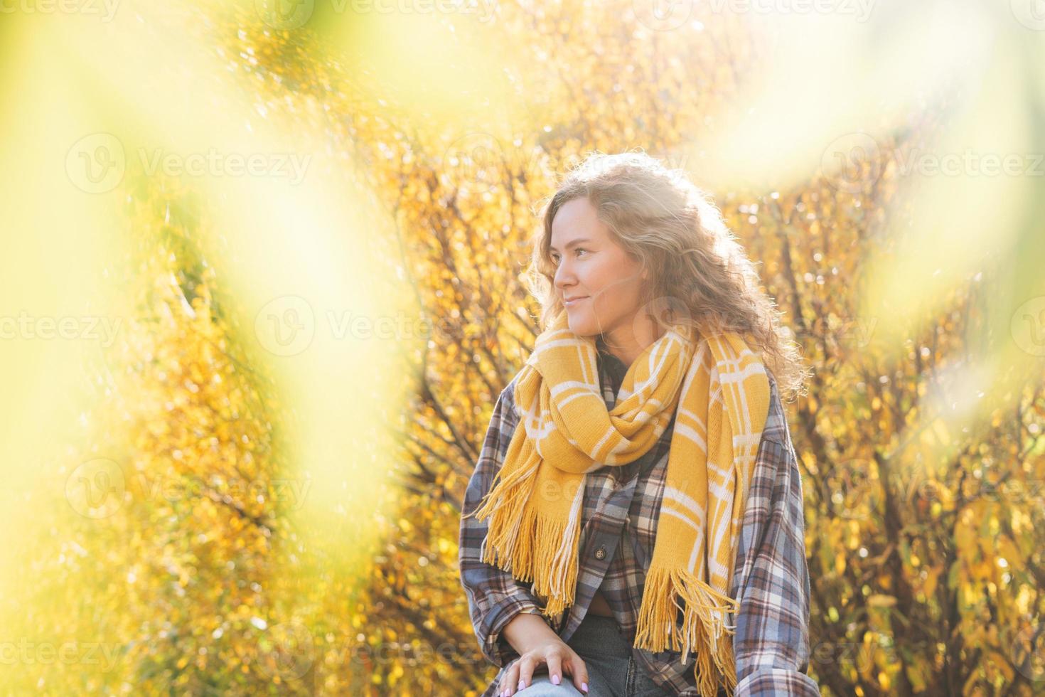 Portrait of Young beautiful woman with curly hair in plaid shirt, jeans and yellow scarf on yellow tree background, hiking on the autumn nature photo