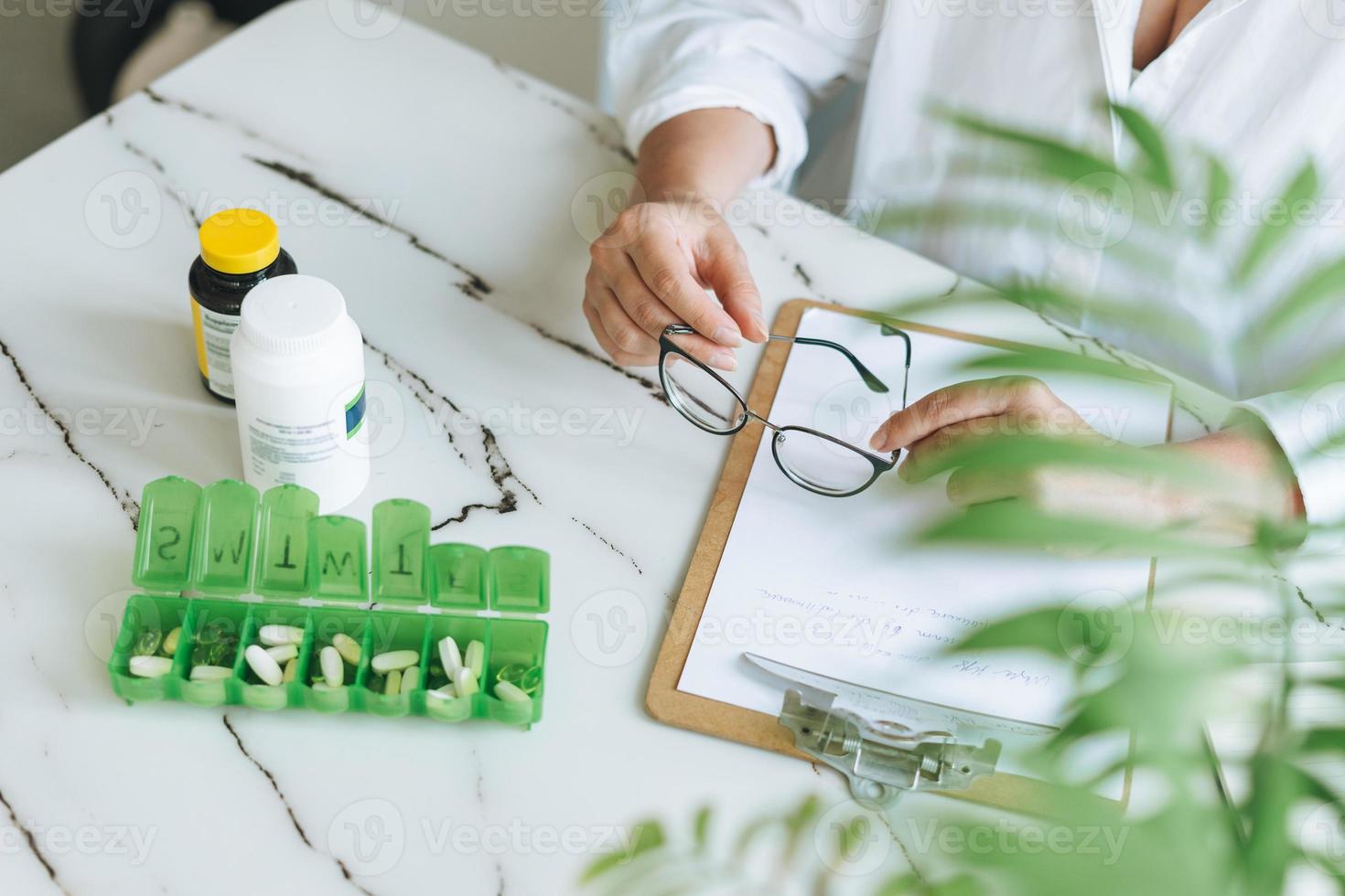 foto recortada de una doctora nutricionista de talla grande con pantalones blanco trabajando en la mesa con pastillas y notas diarias en la moderna y luminosa sala de oficinas