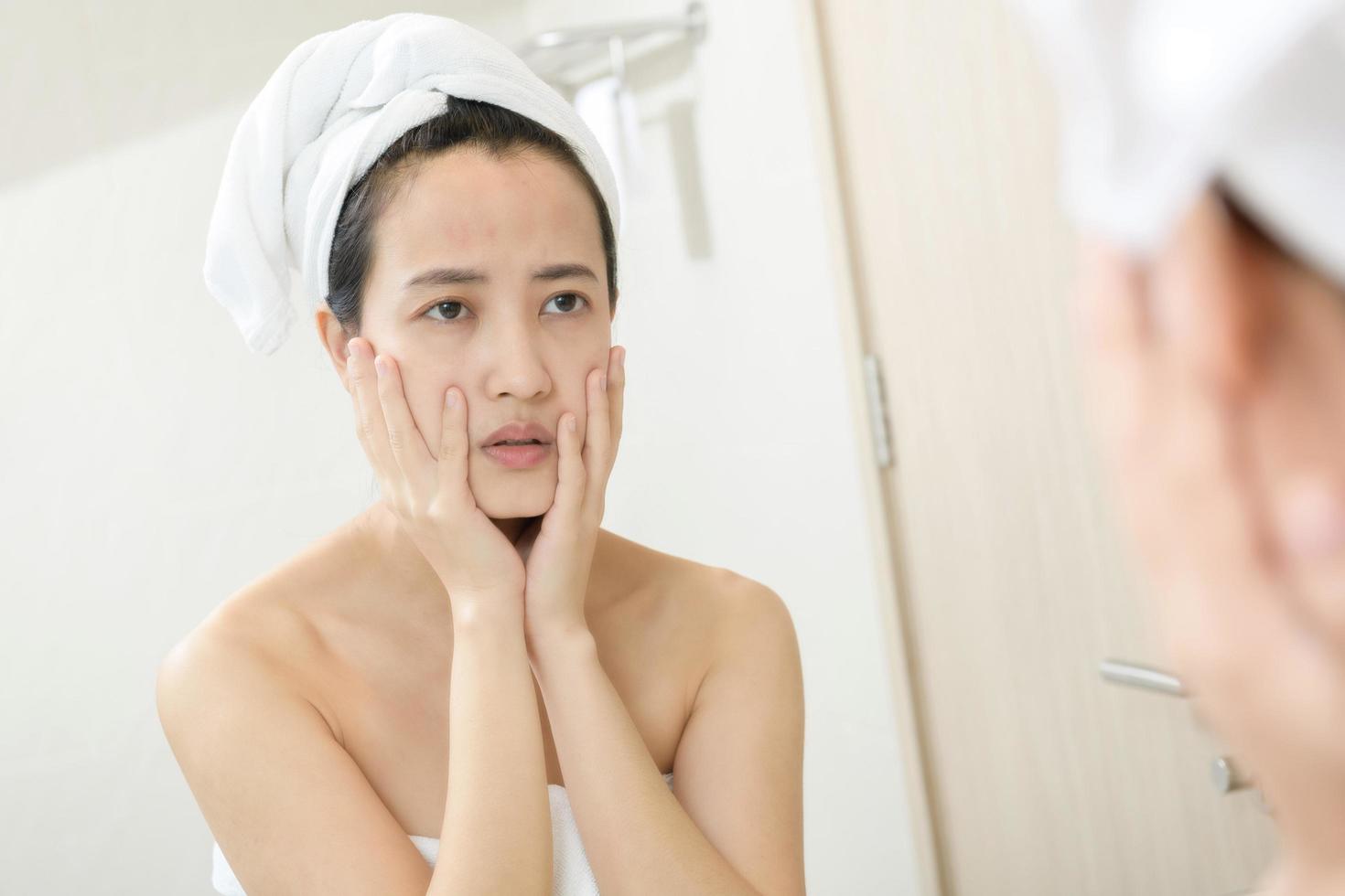 Problem skin. Concerned young asian women popping pimple on cheek while standing near mirror in bathroom. young asian women with acne photo