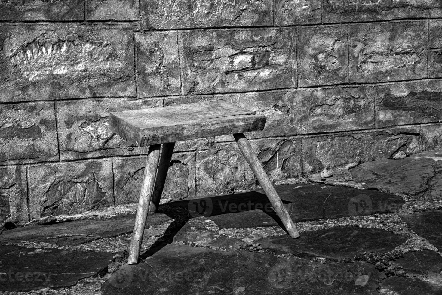 Old small wooden chair in the rural yard near a stone wall. Black and white photo