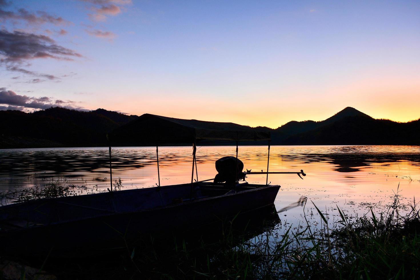 Landscape sunset river with fishing boat and yellow and blue sky twilight beautiful silhouette mountain background photo