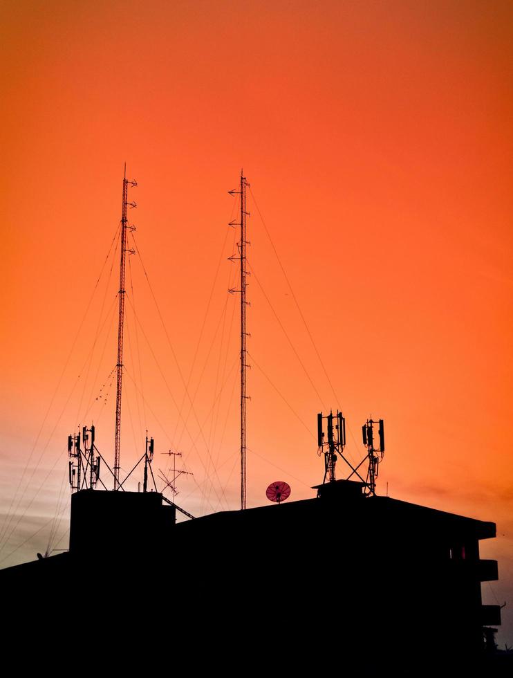 silueta de edificios en la casa con vista al atardecer y torre de radio de comunicación en el cielo naranja foto