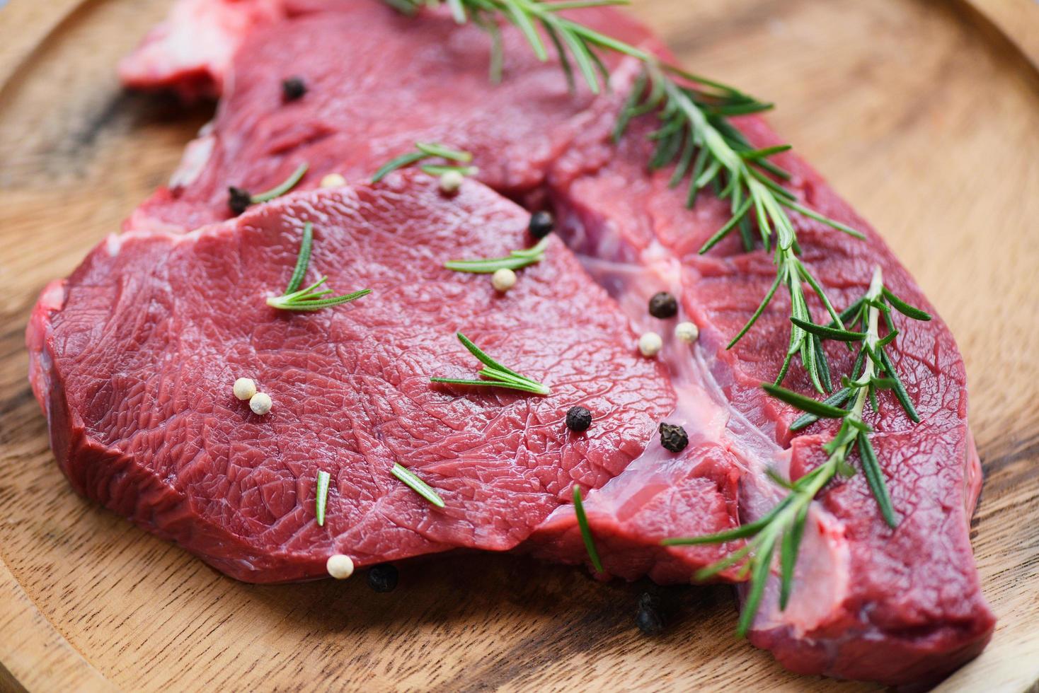 Raw beef meat rosemary on wooden cutting board on the kitchen table for cooking beef steak roasted or grilled with ingredients herb and spices Fresh beef animal protein photo