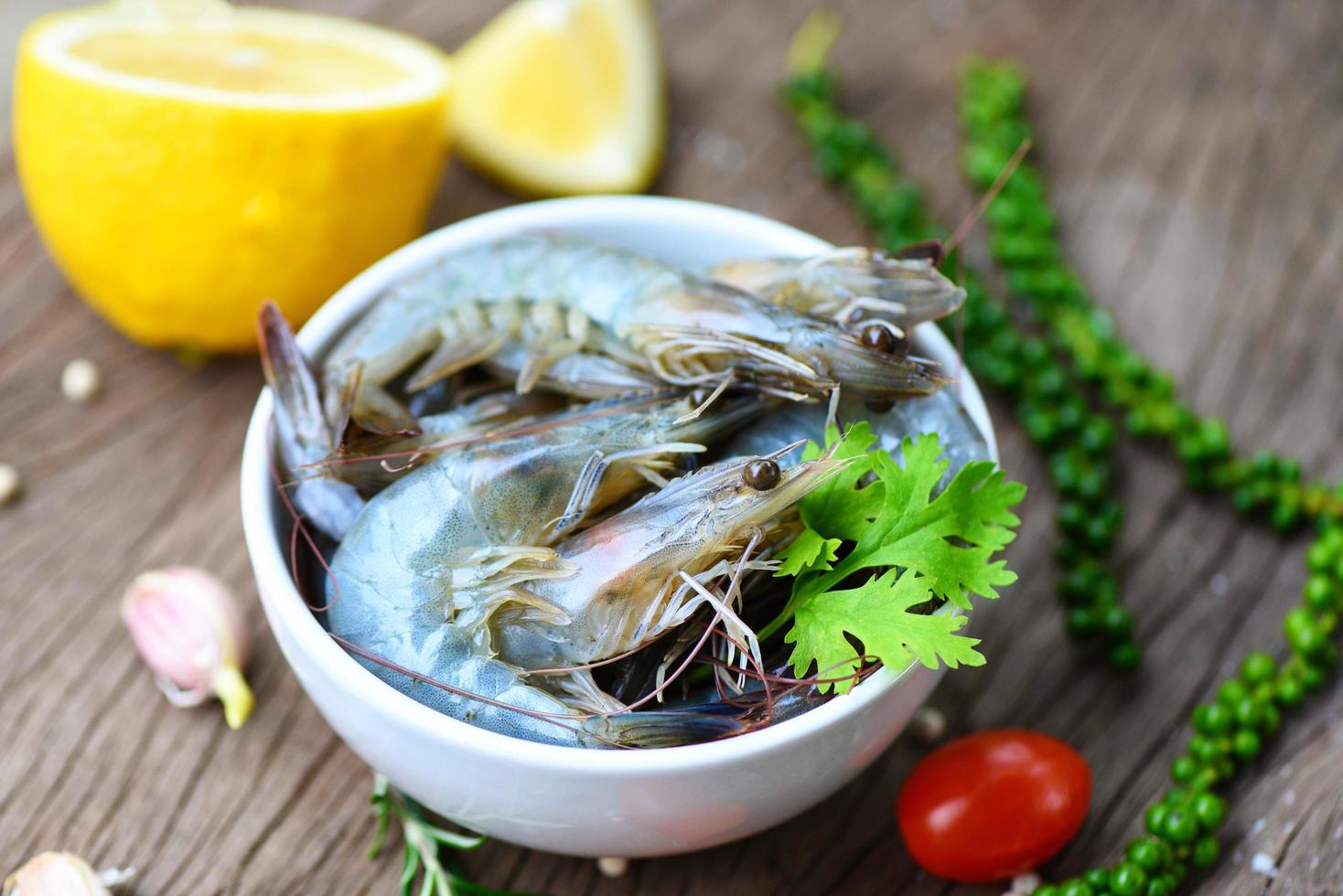 camarones frescos en tazón blanco y fondo de madera con ingredientes hierbas y especias para cocinar mariscos - camarones langostinos crudos foto