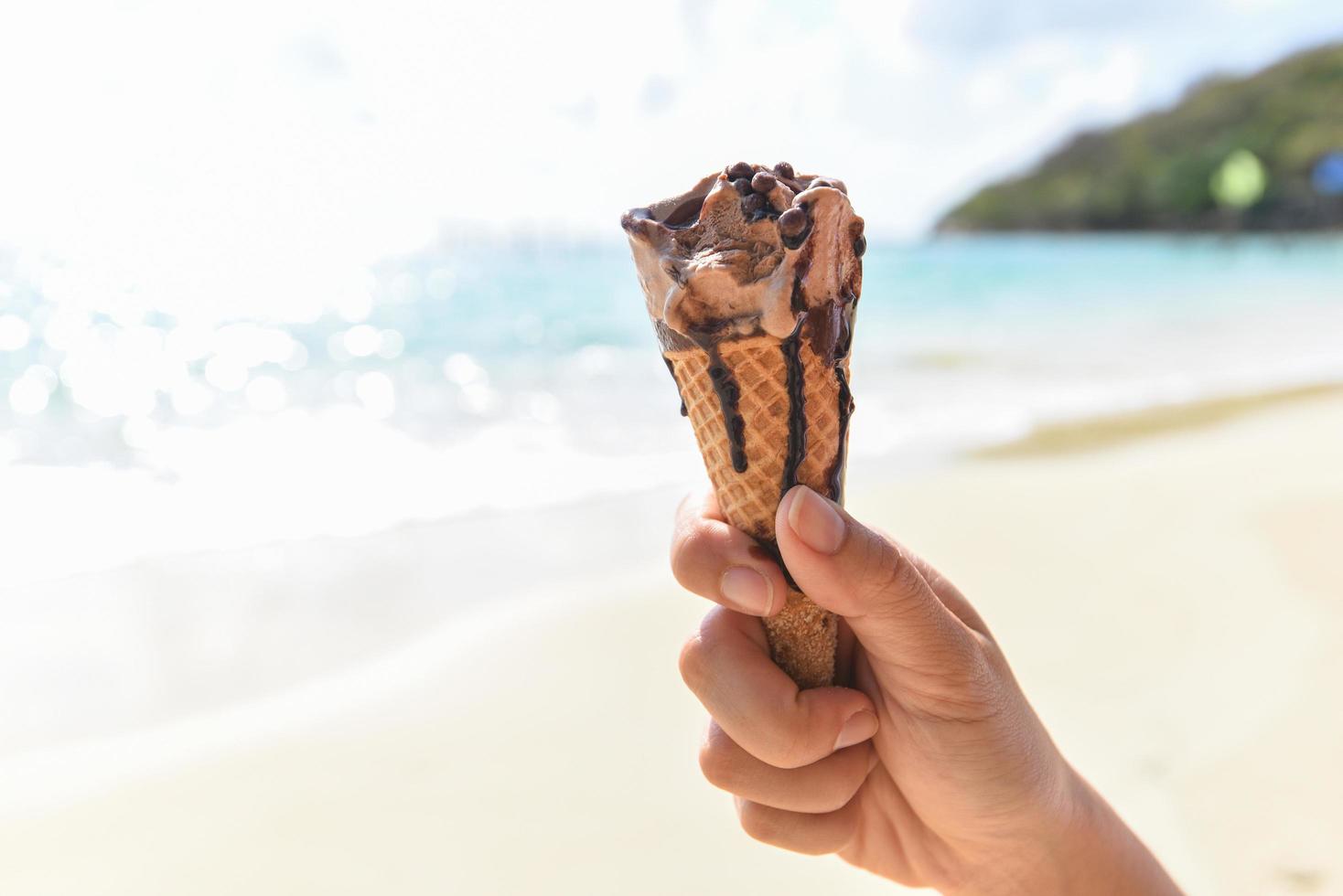 cono de helado en la mano con fondo marino - helado derritiéndose en la playa en verano clima caluroso paisaje oceánico naturaleza vacaciones al aire libre, helado de chocolate foto