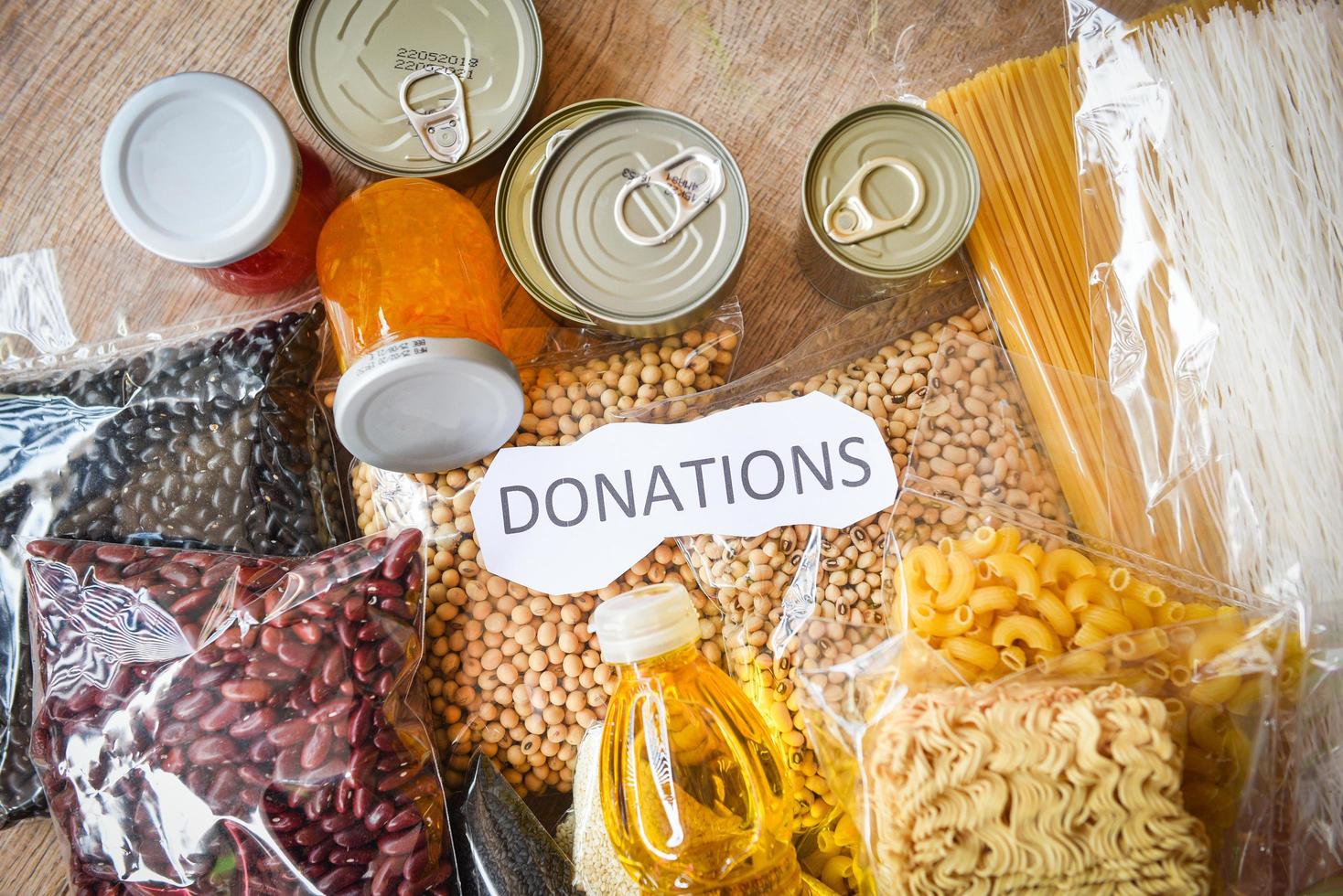 donaciones de comida con comida enlatada en el fondo de la mesa de madera pasta enlatada y comida seca no perecedera con frijoles guisantes aceite de cocina fideos instantáneos macarrones concepto de donación foto