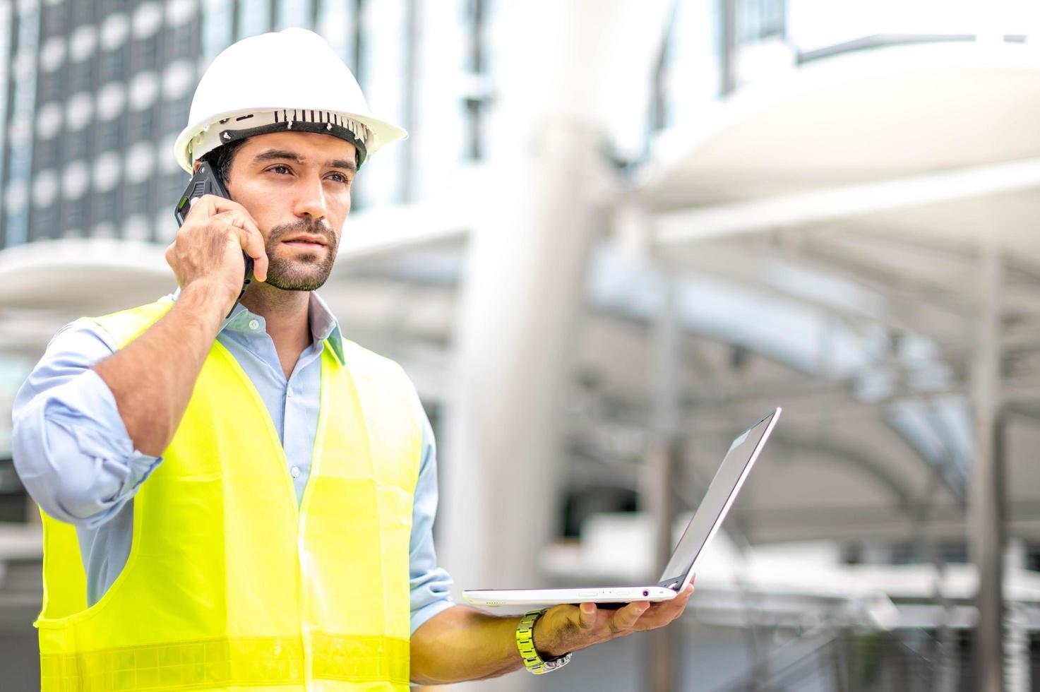 Caucasian man holding smartphone for check situatiob obout the work and the other hand holding laptop prepare to work at the construction site in the city. photo