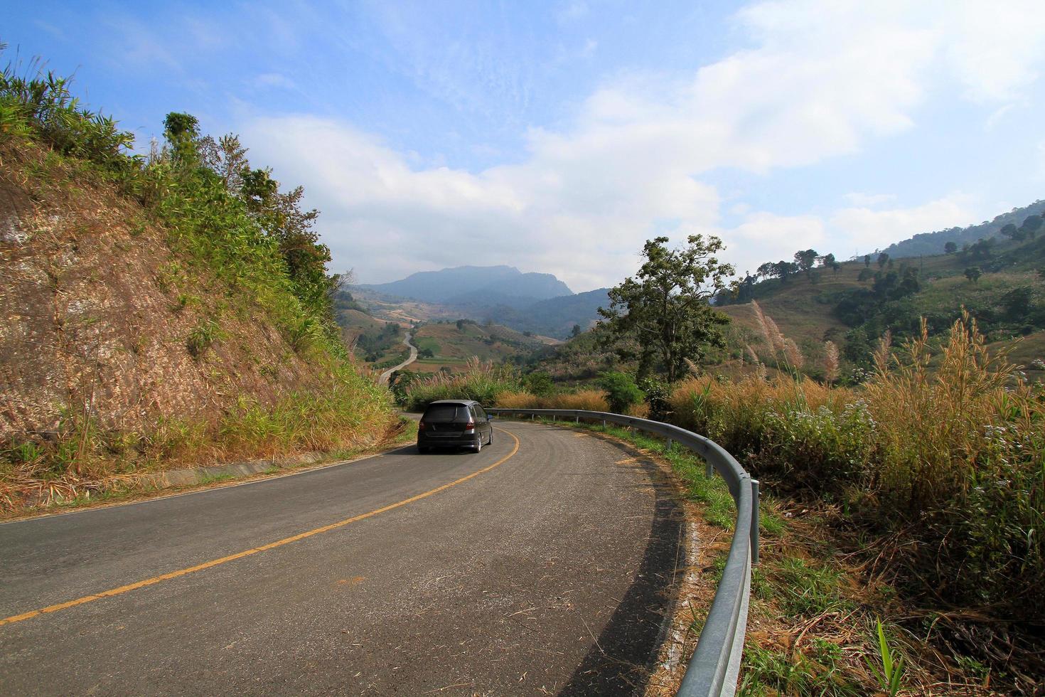 Black car on asphalt road go down and up to hill along with mountains and clouds blue sky background at Phu Lanka Forest Park, Phayao, Thailand. Beauty of natural. Beautiful pathway, Travel and street photo