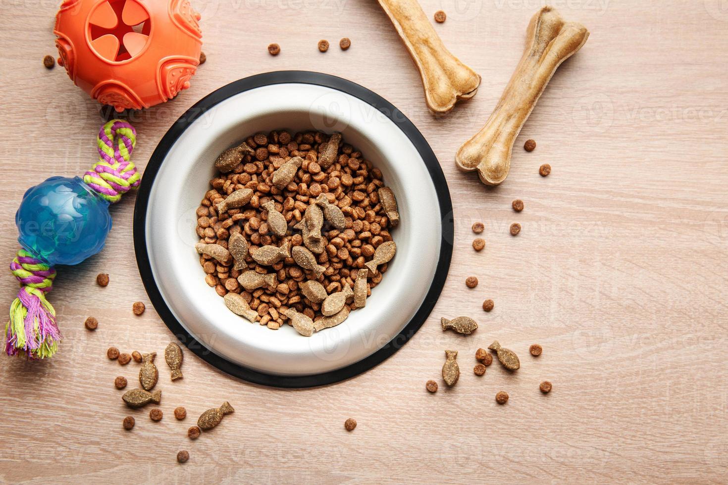 A bowl with dog food, dog treats and toys on a wooden floor. photo