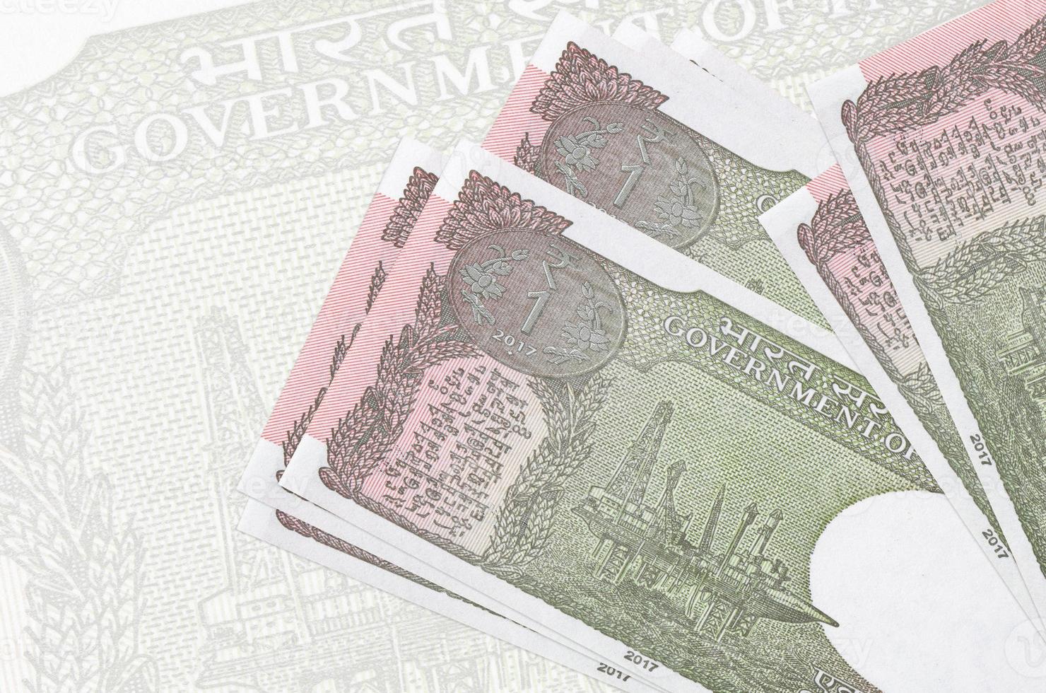 1 Indian rupee bills lies in stack on background of big semi-transparent banknote. Abstract presentation of national currency photo