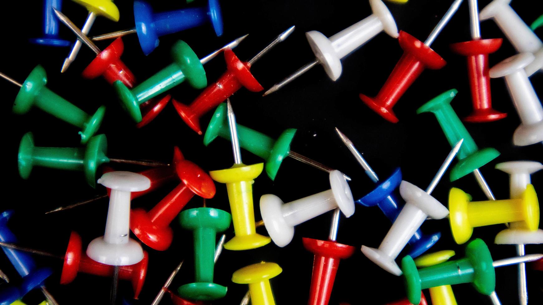 multicolored thumbtacks on a black background photo