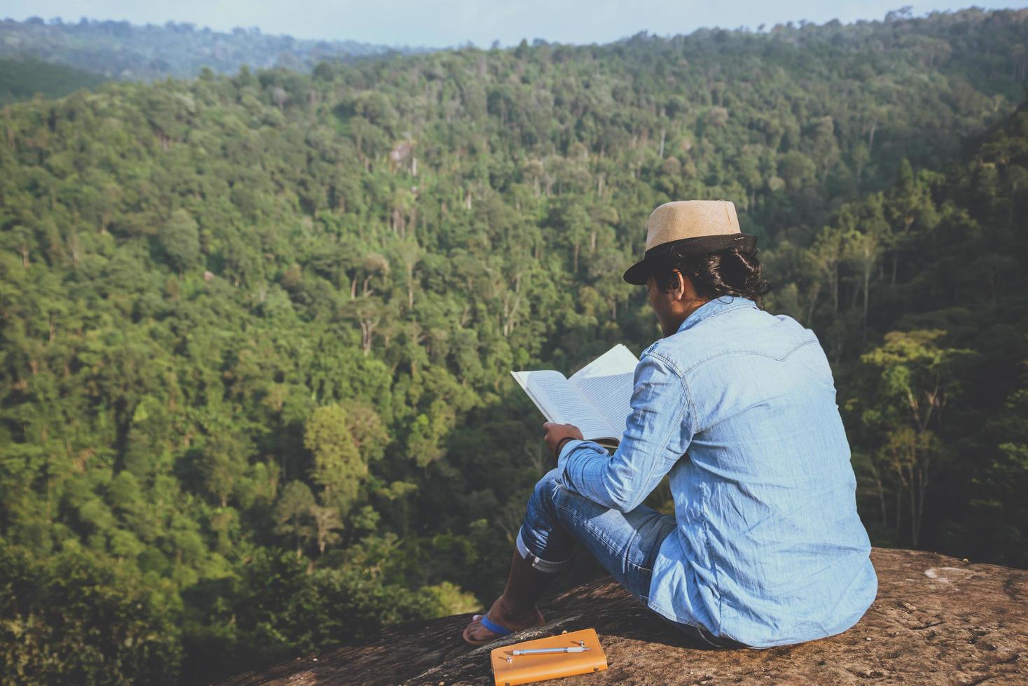 viaje de hombre asiático relajarse en las vacaciones. asientos relajarse leer libros sobre acantilados rocosos. en la montaña. En Tailandia foto