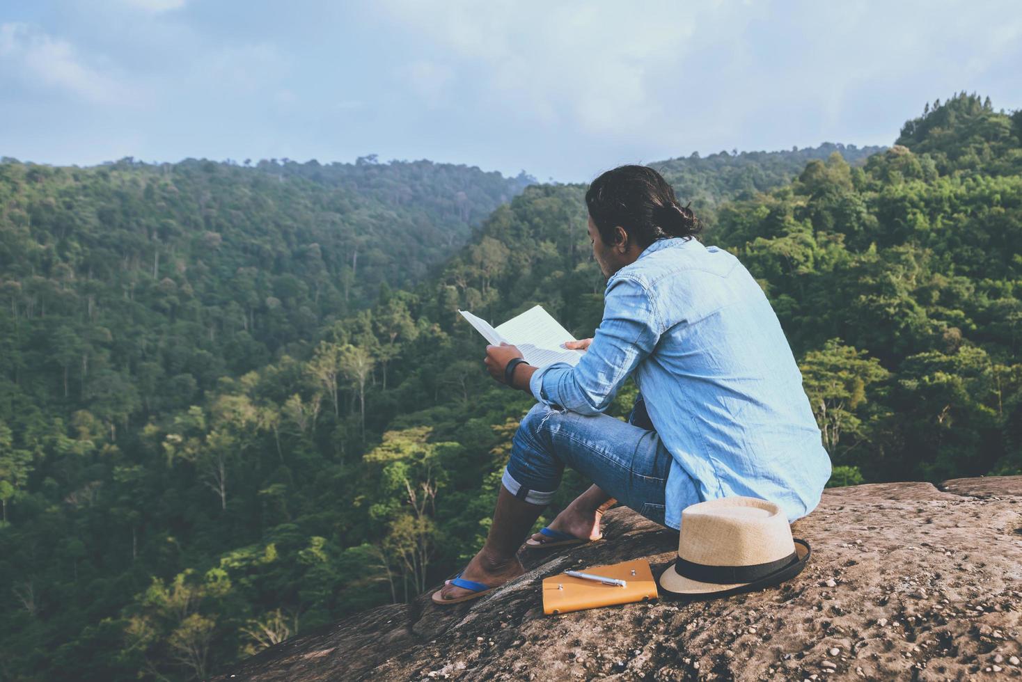 viaje de hombre asiático relajarse en las vacaciones. asientos relajarse leer libros sobre acantilados rocosos. en la montaña. En Tailandia foto