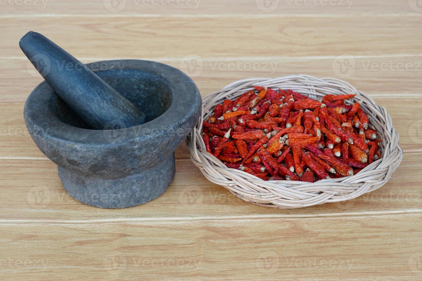 Old granite stone mortar with pestle and basket of red dried chillies for cooking.Concept, kitchen utensils .Thai cooking tool, use to  pound chili paste or curry paste. photo