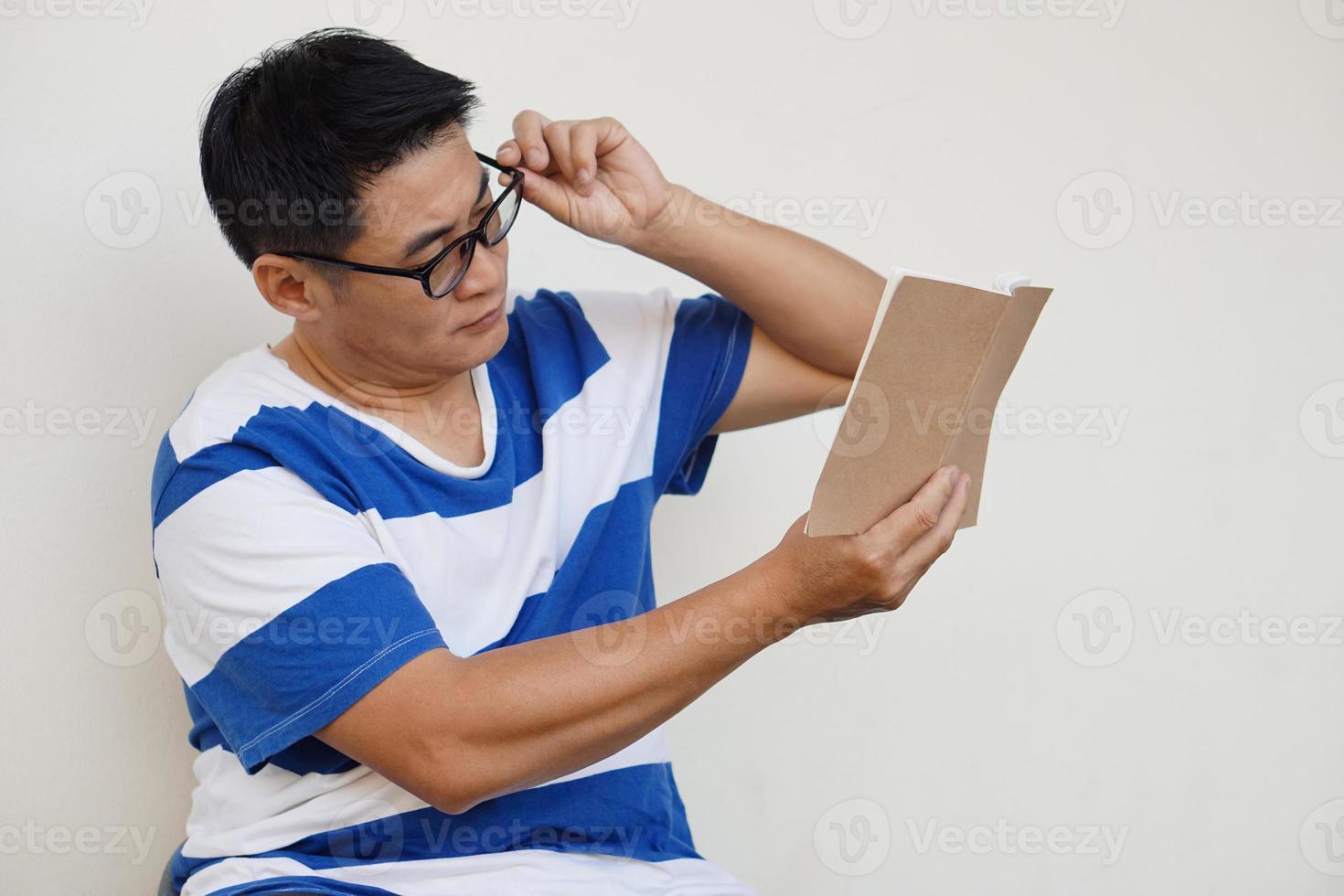 un hombre asiático de mediana edad usa anteojos y está leyendo un libro. concepto, problema de la vista. optometría. anteojos con lentes convexas o cóncavas. miopía.enfermedad ocular foto