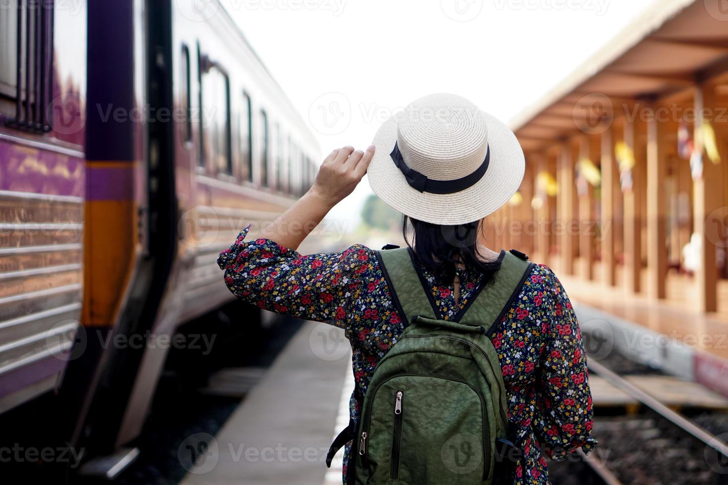 Back view of woman traveller at railway station, wear white hat and backpack. Concept, travel by train in Thailand . Transportation. Alone journey. Weeken, holiday or vacation trip. photo