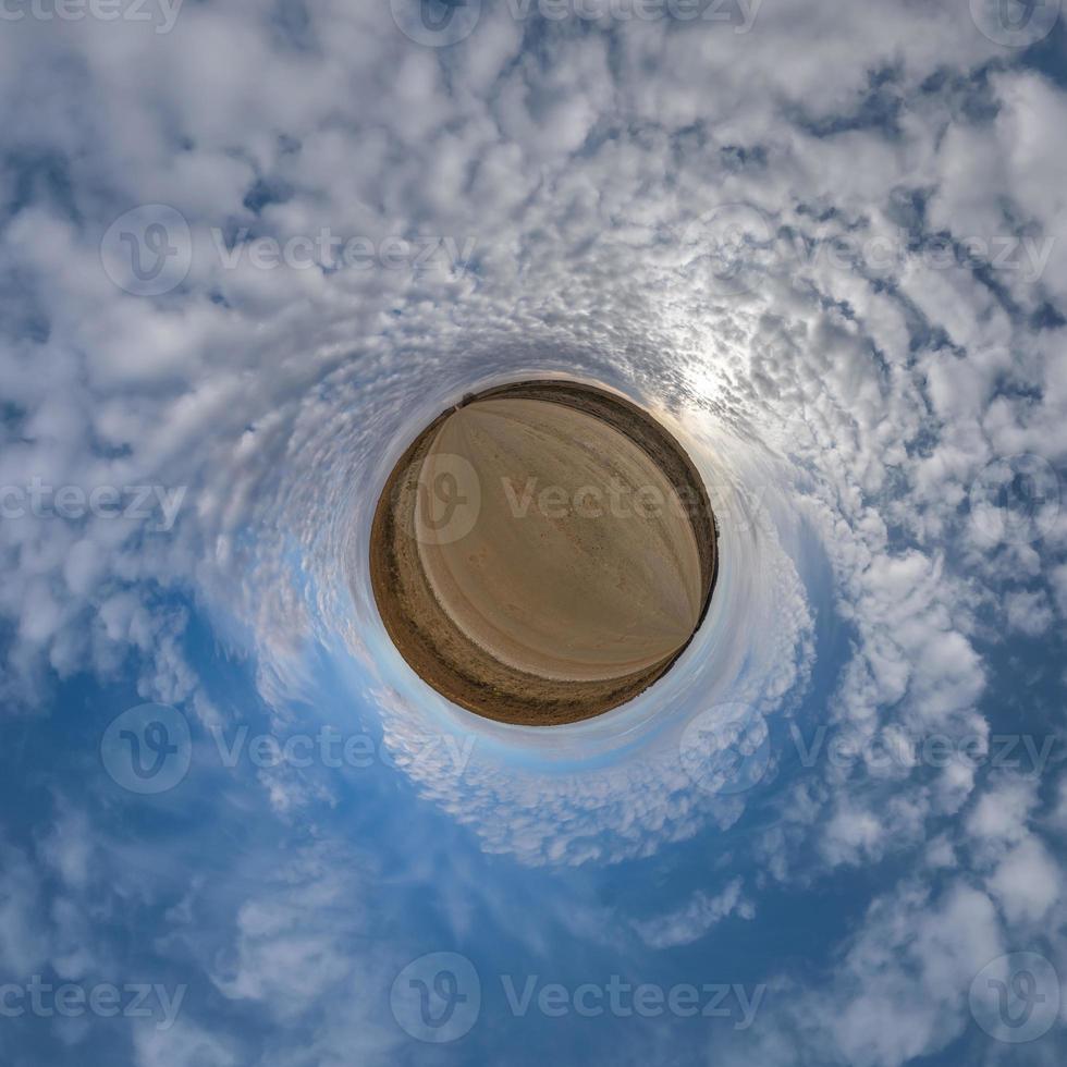 tiny planet in blue overcast sky with beautiful clouds with transformation of spherical panorama 360 degrees. Spherical abstract aerial view. Curvature of space. photo