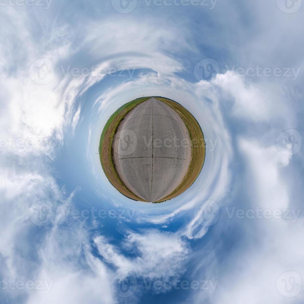 tiny planet in blue overcast sky with beautiful clouds with transformation of spherical panorama 360 degrees. Spherical abstract aerial view. Curvature of space. photo