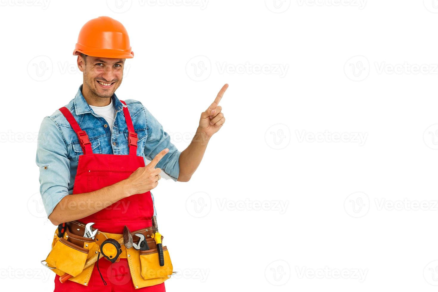 Cheerful male contractor wearing helmet isolated on white background pointing aside while looking at camera photo