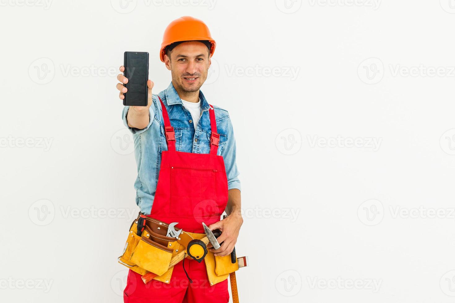 profession, construction and building - happy smiling male worker or builder in helmet and overall with smartphone over white background photo