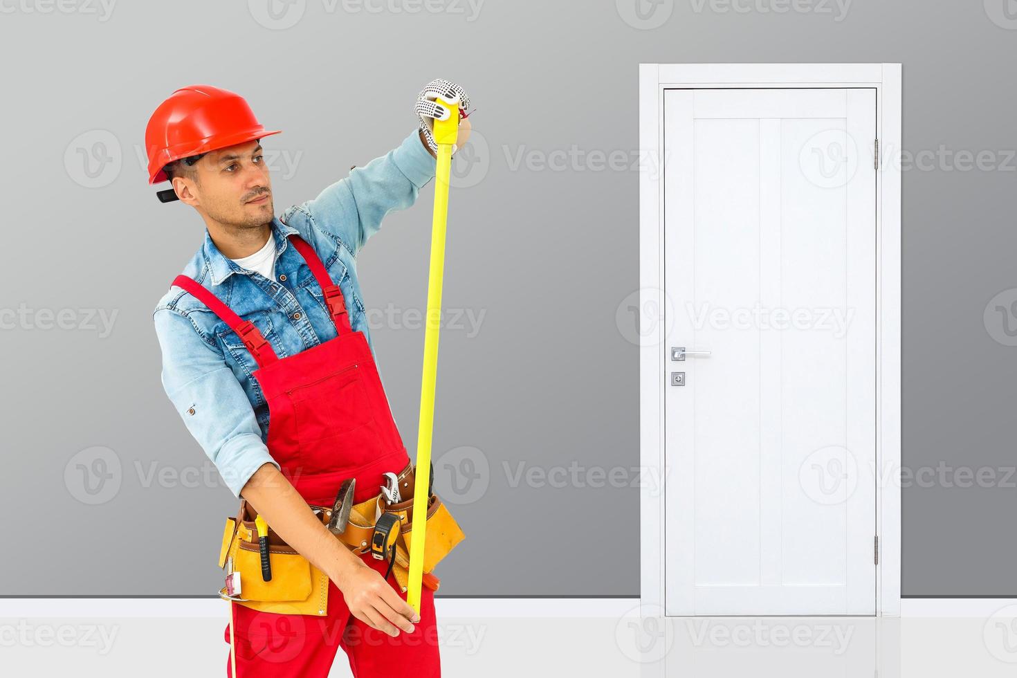 Young handyman installing a white door with an electric hand drill in a room photo