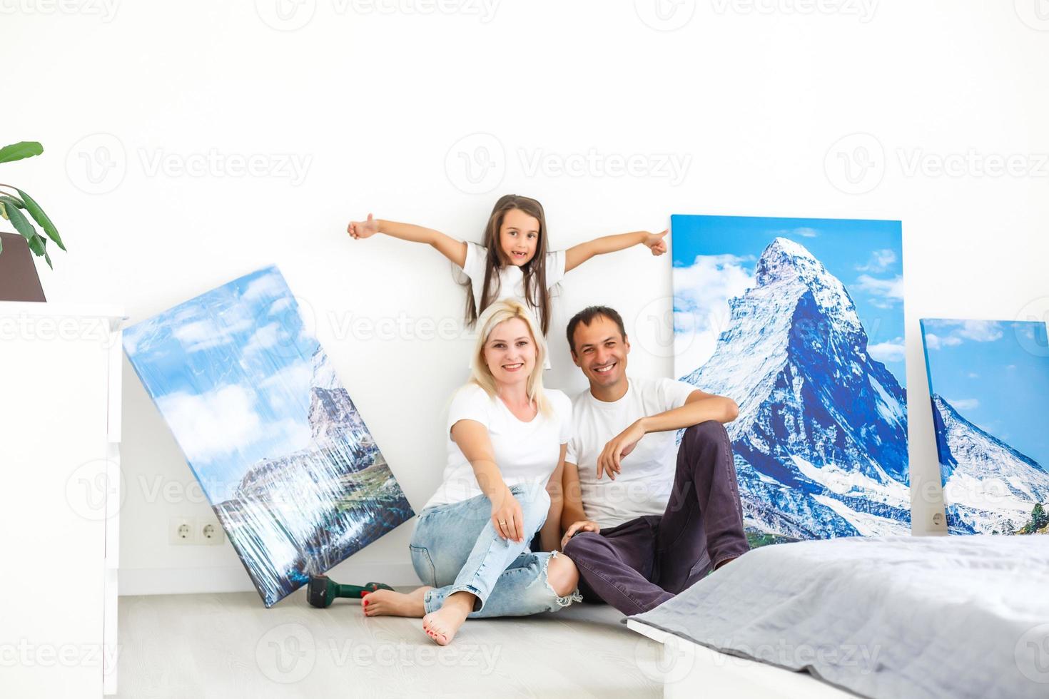 In new flat family hangs a large photo canvas on empty white wall at home