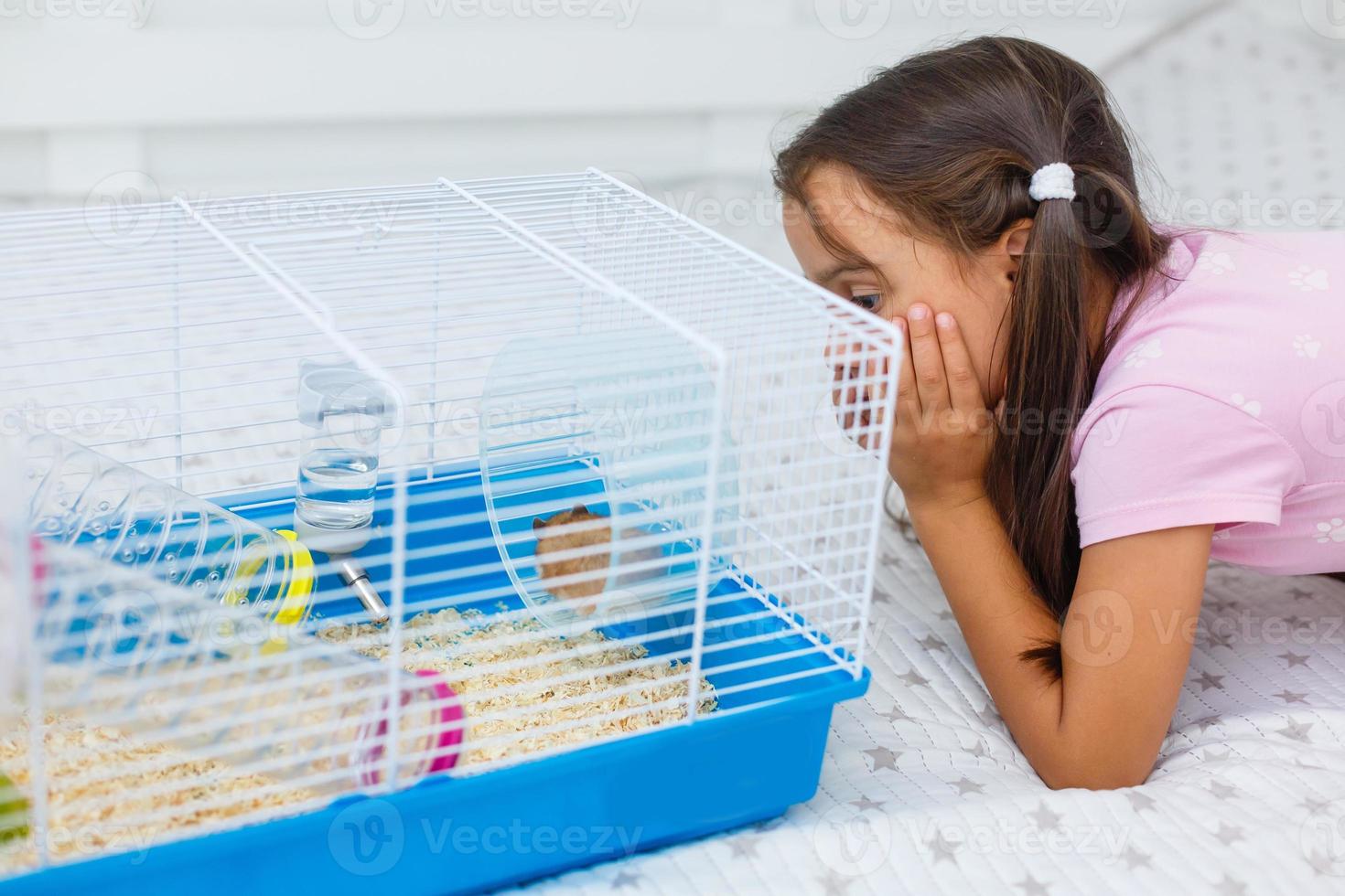 Little girl holds cage for hamster at home photo