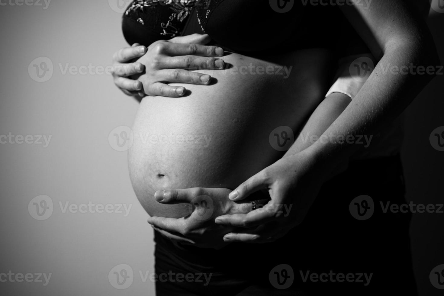 Black and white photo of the hands and belly of a pregnant woman and her husband