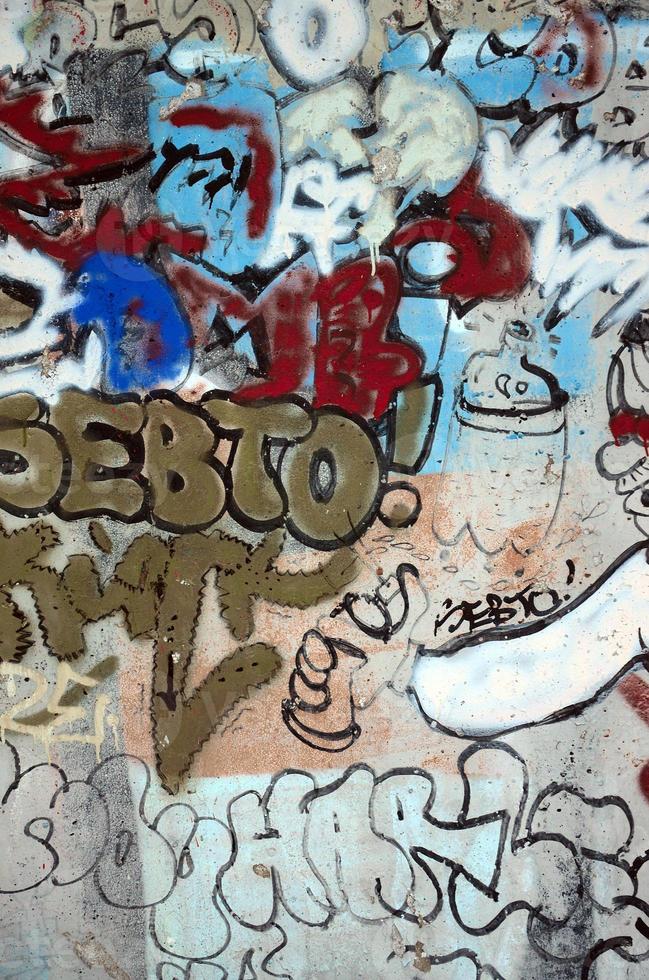 Close-up fragment of a graffiti drawing applied to the wall by aerosol paint. The wall is spoiled by a multitude of colorful signatures and tags from street artists and hooligans photo
