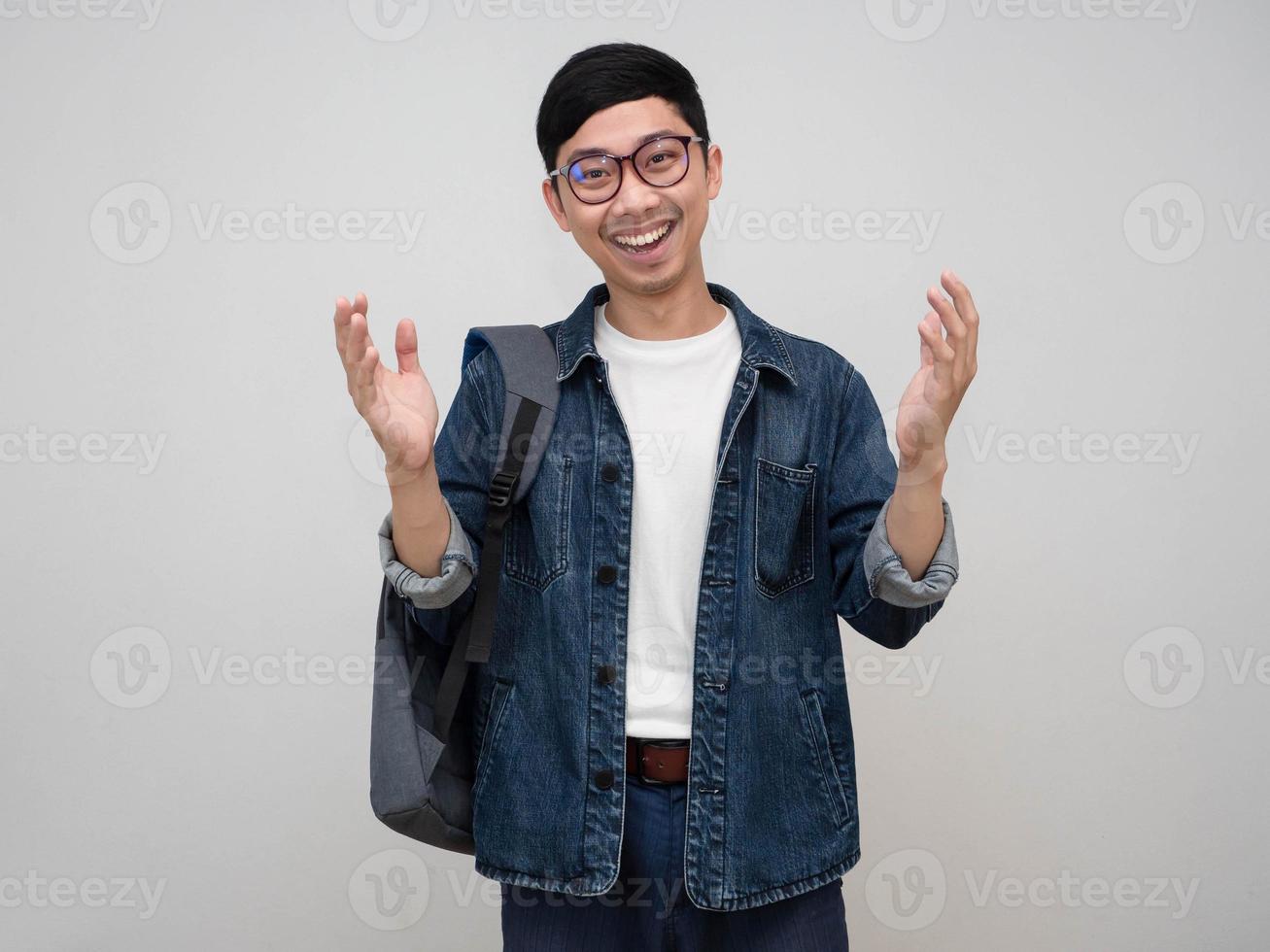 Positive asian man jeans shirt wear glasses carry bag show hands up cheerful smile isolated photo