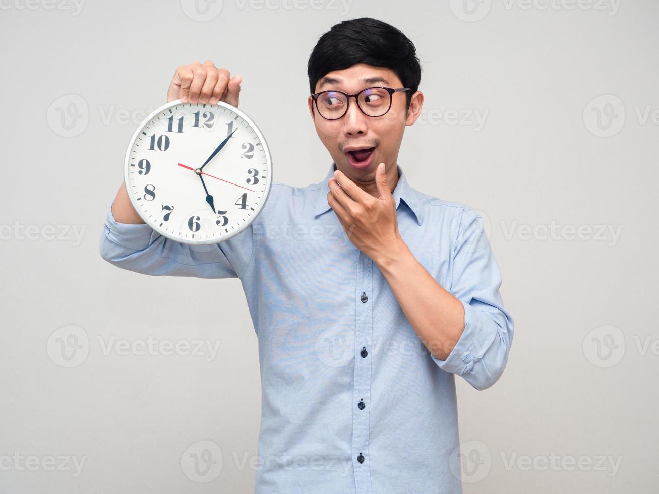 Asian man wear glasses gesture looking at analog clock in his hand isolated photo