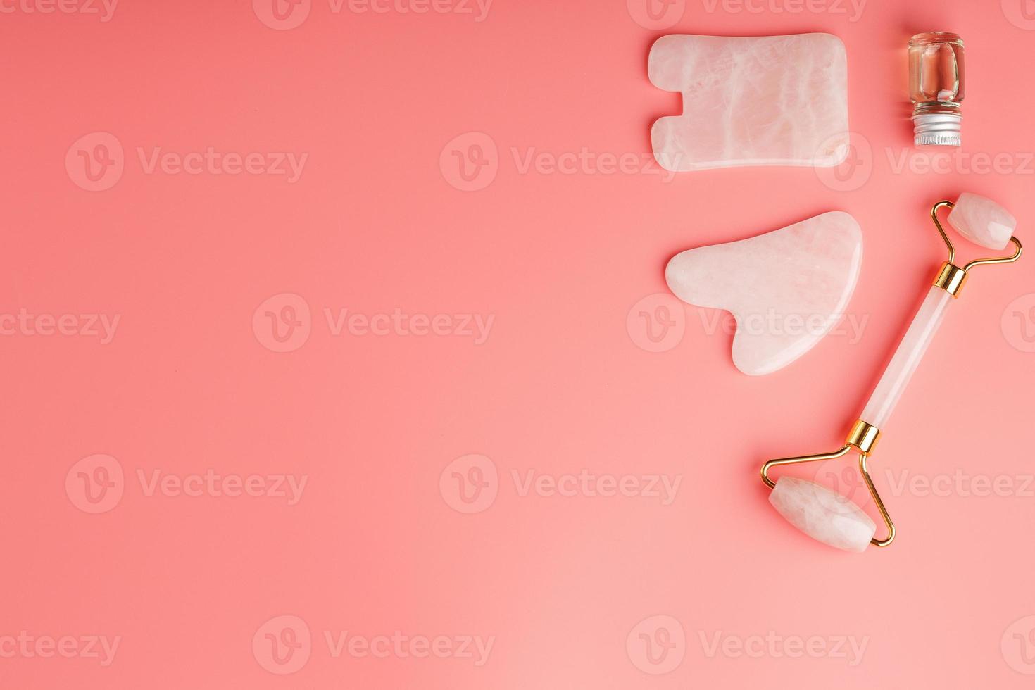 un conjunto de herramientas para la técnica de masaje facial gua sha hechas de cuarzo rosa natural sobre un fondo rosa. rodillo, piedra de jade y aceite en tarro de cristal para el cuidado facial y corporal. foto