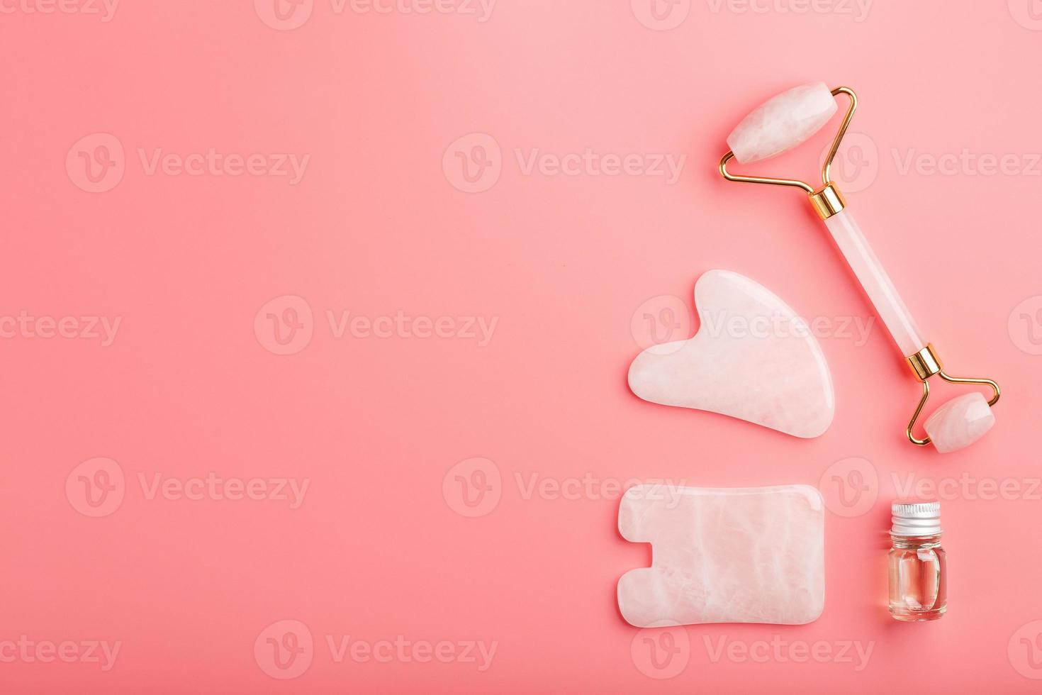 un conjunto de herramientas para la técnica de masaje facial gua sha hechas de cuarzo rosa natural sobre un fondo rosa. rodillo, piedra de jade y aceite en tarro de cristal para el cuidado facial y corporal. foto