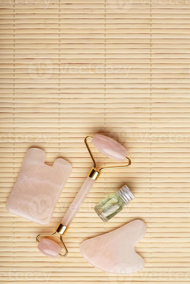 Gua sha massage made of natural rose Quartz-roller, jade stone and oil, on a bamboo background for face and body care. photo