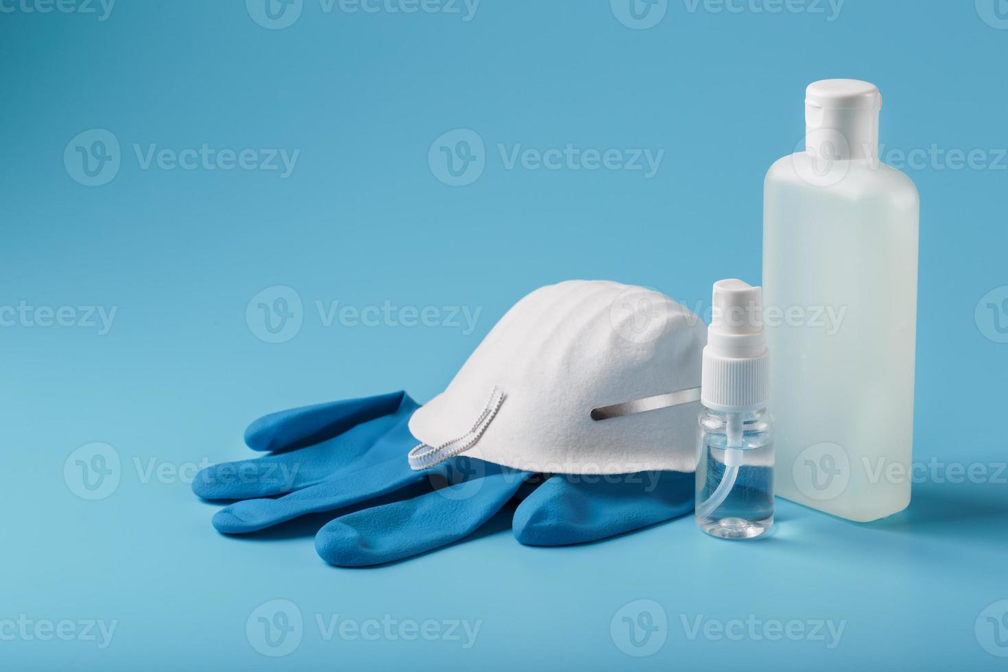 Bodegón de protección antivirus sobre fondo azul, máscara, guantes de goma, una botella de desinfectante para manos, gel antiséptico. foto