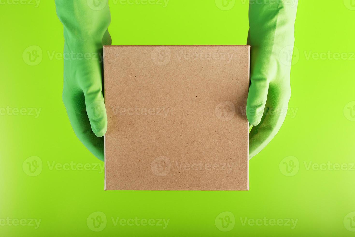 A square box in the hands with green rubber gloves on a green background. photo