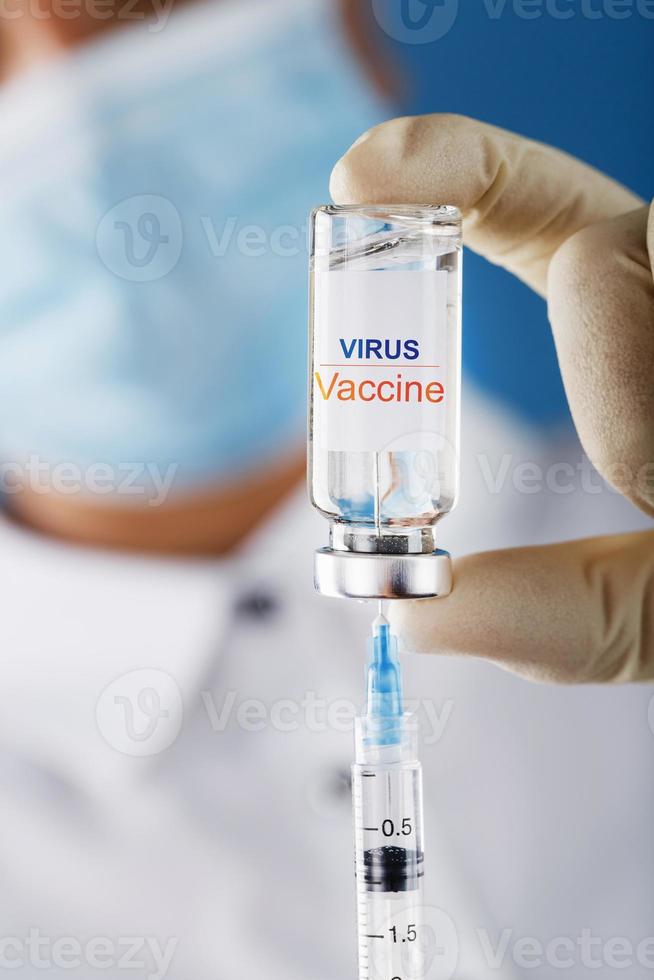 una ampolla con la vacuna del virus de la inscripción y una jeringa en manos de un médico científico con guantes de goma con un primer plano de la vacuna. foto
