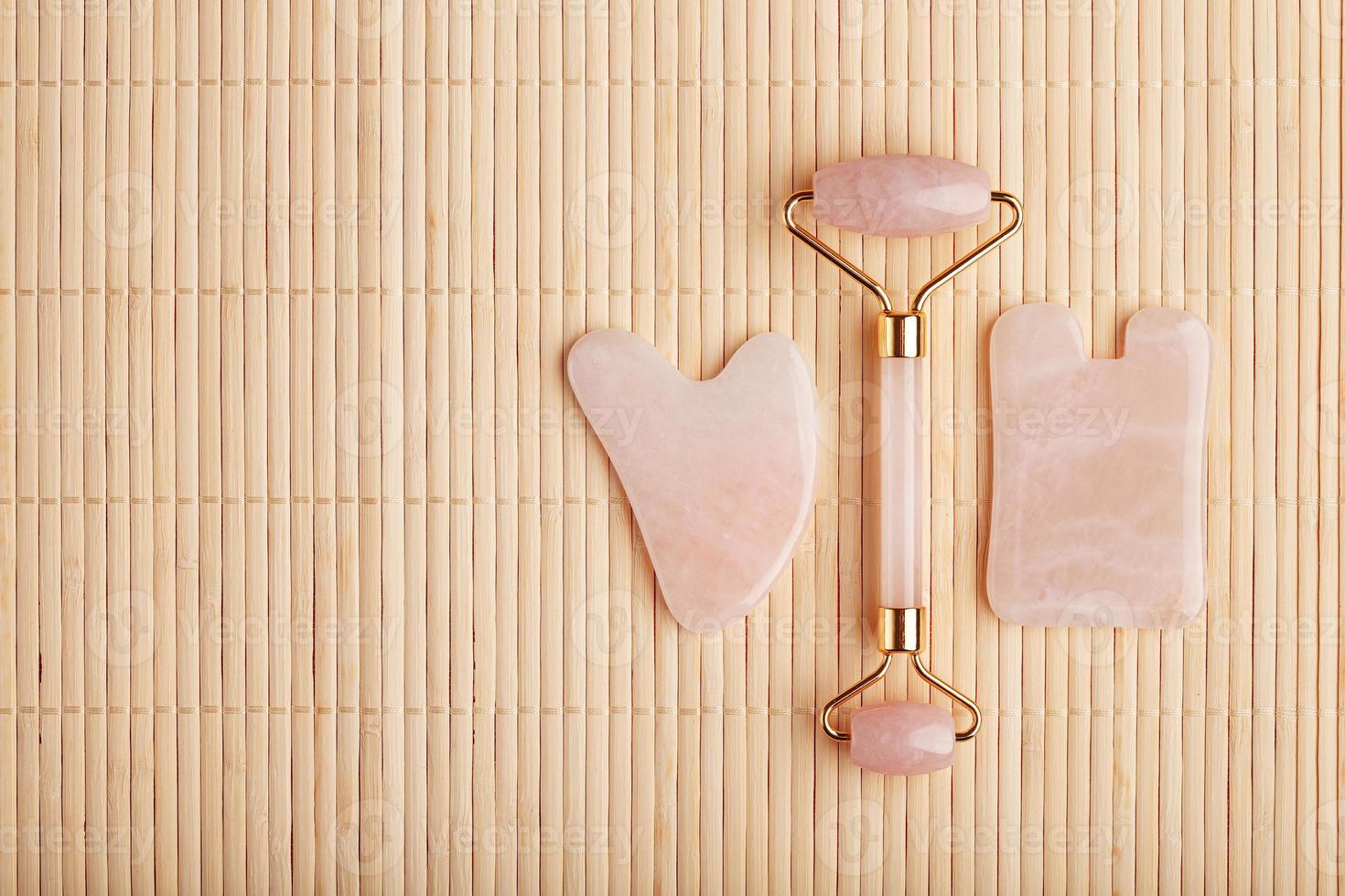 un conjunto de herramientas para la técnica de masaje facial gua sha fabricado en cuarzo rosa natural. rodillo, piedra de jade y aceite en un frasco de vidrio, sobre un fondo de paja para el cuidado de la cara y el cuerpo. foto