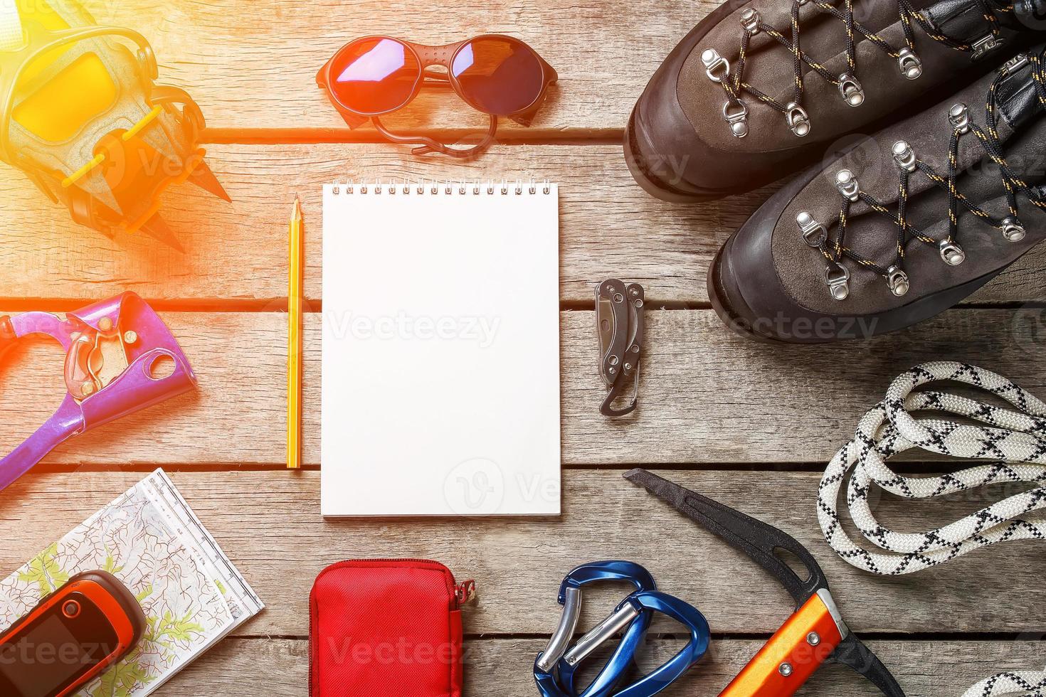 Top view of tourist equipment for a mountain trip on a rustic light wooden floor with a notebook and an empty space in the middle. photo